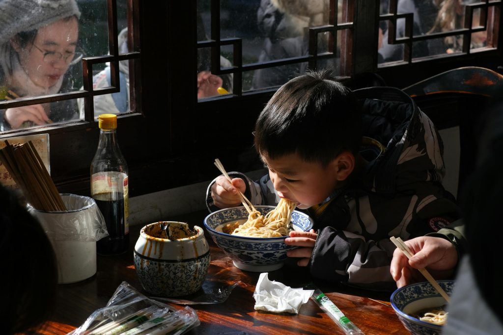 Photo of a Child Eating Noodles with Chopsticks