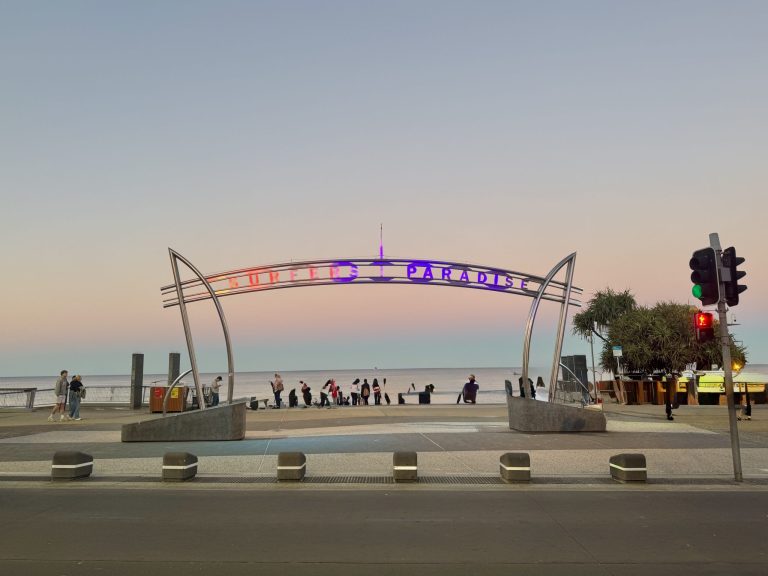 Surfers Paradise sign, with beach in the background and the sun setting