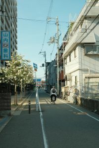 A cyclist rides through a serene street in Suita, Osaka, Japan, on a sunny day.