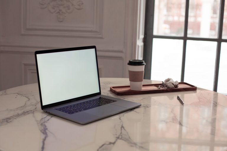 a laptop on a marble top table beside a plastic cup of coffee